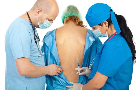 Анестезиологи осматривают спину женщины, чтобы сделать эпидуральную анестезию при кесаревом сечении.