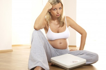 Беременная женщина с весами: скачки веса могут служить признаком внутренних отеков у беременных.
