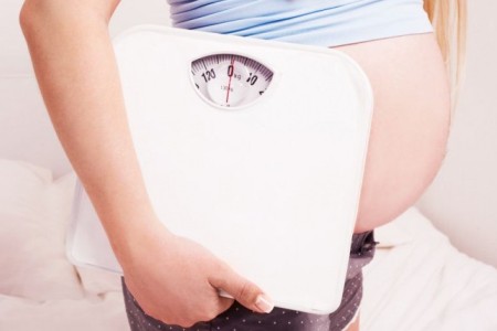 Беременная женщина держит весы: снижение веса - один из предвестников родов.