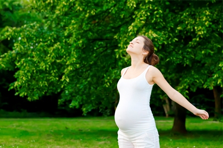 Беременная на природе выполняет дыхательные упражнения. 