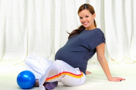 Беременная делает упражнения с мячом.