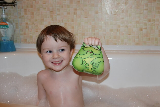 Ребенок играет в ванной и держит в руках игрушку мочалку