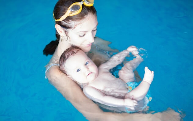 Малыш купается в бассейне в подгузниках